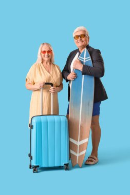 Elinde bavul ve sörf tahtası olan olgun iş adamları mavi arka planda yaz tatiline hazır.