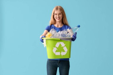 Mavi zemin üzerinde plastik olan geri dönüşüm kutusunu tutan gönüllü bir kadın.