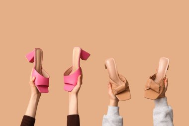 Kahverengi arka planda farklı tarz sandaletleri olan kadın elleri.