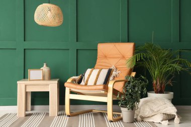 Yastıklı şık bir koltuk, sehpa ve oturma odasındaki yeşil duvarın yanındaki bitkiler.