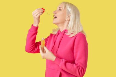 Sarı arka planda CBD yağı alan olgun bir kadın.