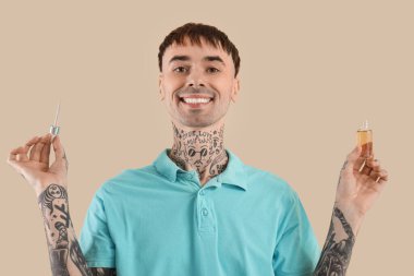 Young tattooed man with bottle of CBD oil on beige background clipart
