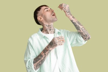 Genç dövmeli adam yeşil arka planda CBD yağı alıyor.