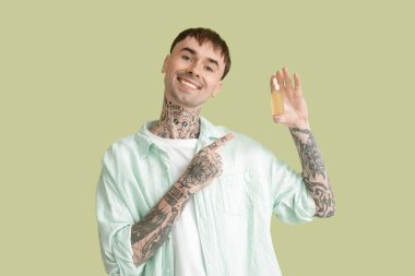 Genç dövmeli adam yeşil arka planda bir şişe CBD yağını işaret ediyor.