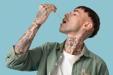 Genç dövmeli adam mavi arka planda CBD yağı alıyor, yakın plan.