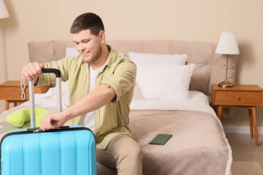 Otel odasında bavullu bir erkek turist oturuyor.