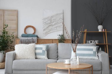 Kanepesi ve vazolarında söğüt dalları olan modern oturma odasının içinde.