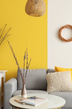 Şık oturma odasındaki masasında söğüt dalları ve dergileri olan vazo.