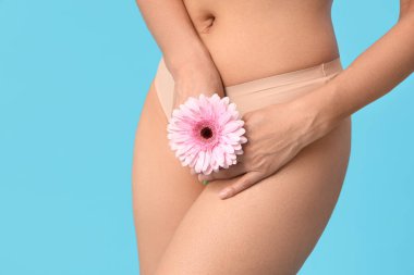 İç çamaşırlı, mavi arka planda Gerbera çiçeği olan güzel bir kadın. Yakın plan.