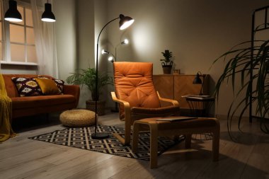 Koyu renk oturma odasının içinde geceleri lambalar ve koltuklar parlıyor.