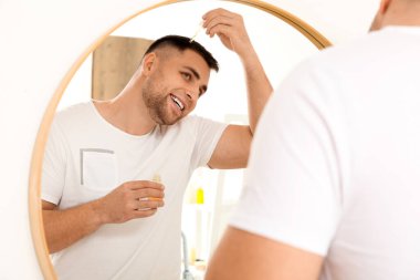 Genç adam banyoda aynanın yanında saç uzatmak için serum kullanıyor.
