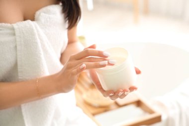 Evdeki banyoda bir kavanoz saç maskesiyle güzel genç bir kadın, yakın plan.