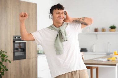 Kulaklıklı genç adam mutfakta müzik dinliyor.