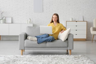 Oturma odasında dizüstü bilgisayarla sohbet eden genç bir kadın.