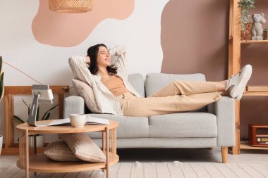 Evdeki gri kanepede yatan genç kadın.