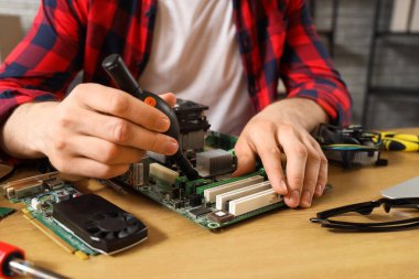 Male technician repairing computer board at table in service center, closeup