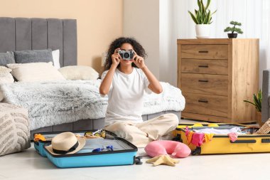 Kameralı güzel genç bir kadın. Evdeki bavullardan yaz kıyafetlerini çıkarıyor.