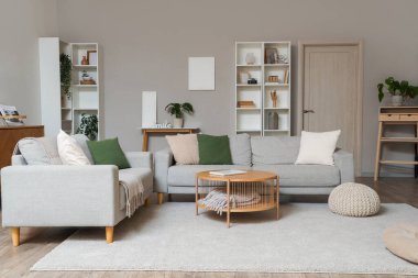 Gri kanepeleri, masası ve raf üniteleri olan modern oturma odasının içinde.