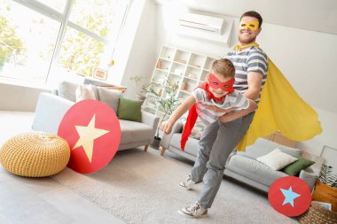 Little boy with his father in superhero costumes having fun at home clipart