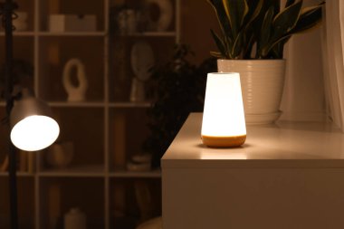 Odadaki çekmecelerin yanındaki saksıda parlayan lamba, yakın plan.