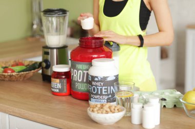 Evde blender 'da protein içeceği hazırlayan genç bir kadın, yakın plan.