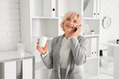 Ofiste telefonla konuşan, bir bardak su içen olgun bir iş kadını.
