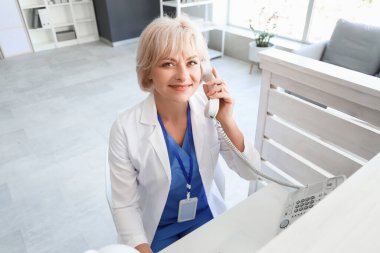 Klinikteki resepsiyonda telefonla konuşan kadın doktor.