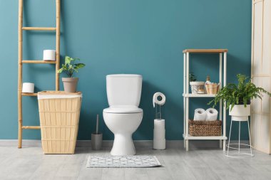 Tuvalet, çöp tenekesi, merdiven ve raf ünitesi mavi duvarın yanında.