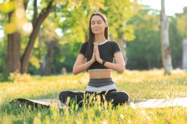Parktaki yoga minderi üzerinde meditasyon yapan genç bir kadın.