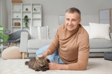 Olgun bir adam evde sevimli bir kediyi okşuyor.