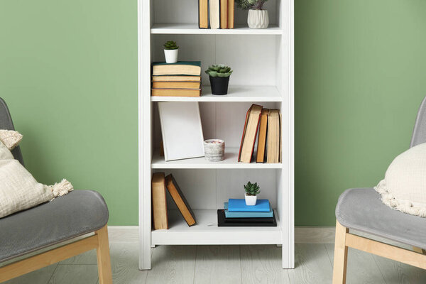 Bookcase with books and houseplants near cozy armchairs in living room, closeup