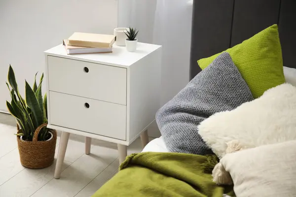 stock image Bedside table with books near cozy bed in bedroom