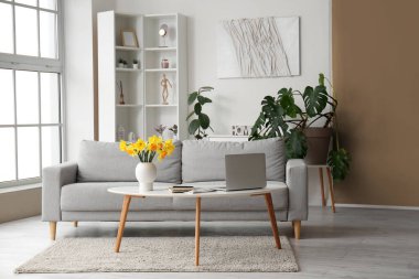 Modern dizüstü bilgisayarı sehpada ve gri koltuğu olan şık bir oturma odası.