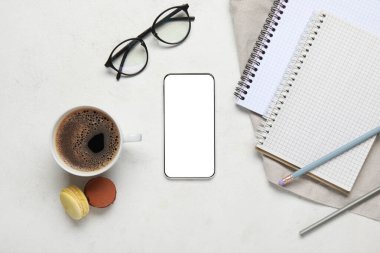 Cep telefonu, kırtasiye malzemesi ve açık arkaplanda bir fincan kahve ile kompozisyon