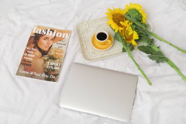 Güzel ayçiçekleri, bir fincan kahve, dergi ve hafif kumaşlı modern dizüstü bilgisayar.