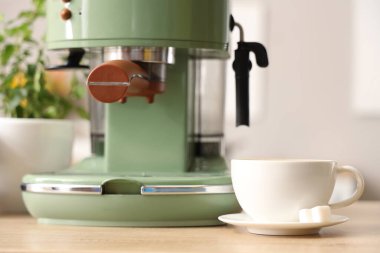 Modern kahve makinesinin yanında şekerli bir fincan espresso, ahşap masa, yakın plan.