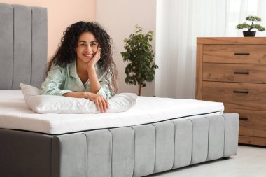 Yatak odasındaki yumuşak yatakta yastıklı genç Afro-Amerikalı kadın.