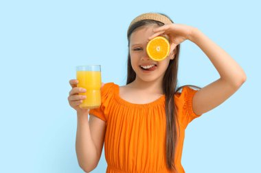 Mavi arka planda portakal suyu bardağı olan küçük bir kız.