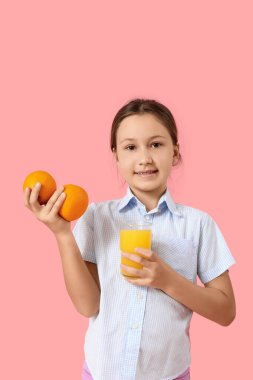 Portakalları ve pembe arka planda bir bardak meyve suyu olan tatlı küçük bir kız.