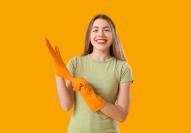 Turuncu arka plana lastik eldiven takan genç bir kadın.