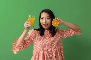 Yeşil arka planda portakal suyu ve bir bardak meyve suyu olan güzel Asyalı kadın.