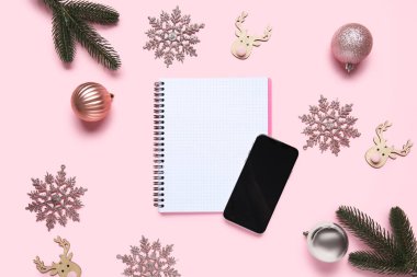 Cep telefonu, defter ve pembe arka planda güzel Noel süslemeleri olan kompozisyon