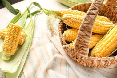 Beyaz masada taze mısır koçanları olan bir sepet.