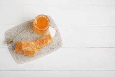 Bir kavanoz tatlı bal, kepçe ve hafif ahşap arka planda taraklar.