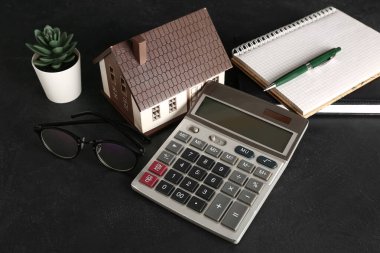 Siyah arkaplanda ev modeli, hesap makinesi, defter ve gözlük