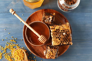 Mavi ahşap arka planda bal, tarak ve arı poleni olan bir kase.