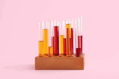 Tahtadan yapılmış renkli numunelerle test tüpleri pembe arka planda duruyor.