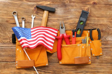 Farklı aletlere sahip kemer ve ahşap arka planda Amerikan bayrağı. İşçi Bayramı kutlamaları