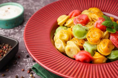 Bir tabak kaynamış renkli hamur köftesi, fesleğen ve bir kase ekşi krema.