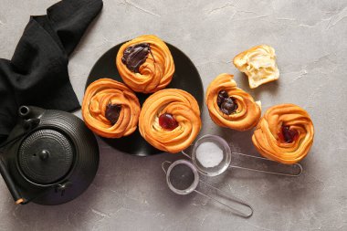 Gri zemin üzerinde çikolata, reçel ve çaydanlık bulunan lezzetli kabuklu tabaklar.